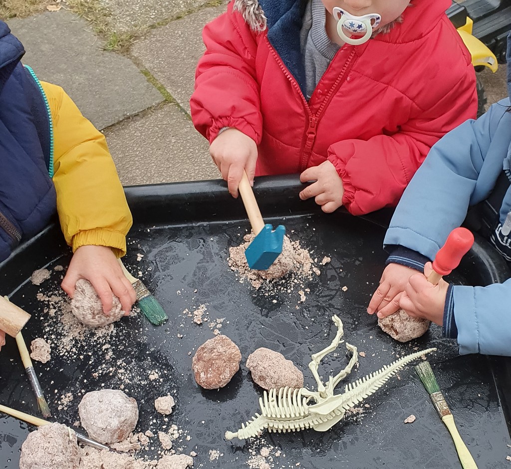 Children playing archaeologist, uncovering dinosaur skeletons from stones with wooden tools