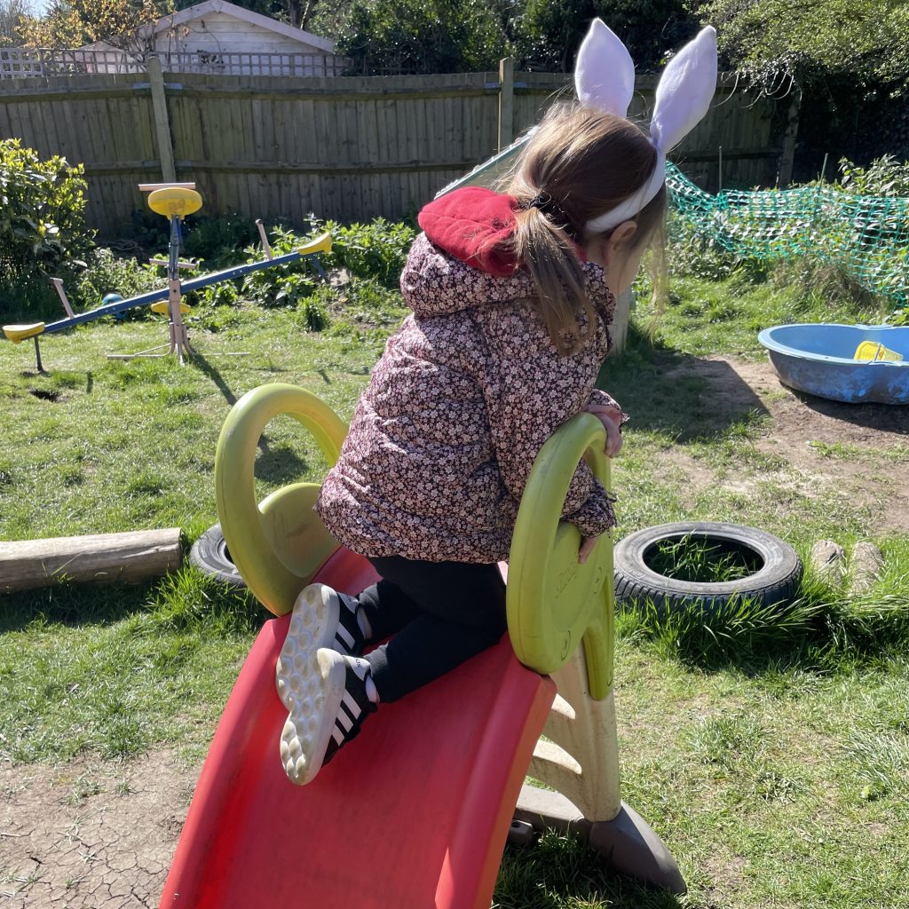 Girl going down a red slide in the garden, wearing a winter jacket