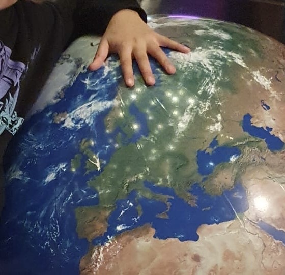 Child's hand resting on top of a large globe showing Europe